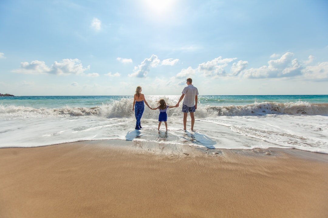A family is standing on the beach holding hands.